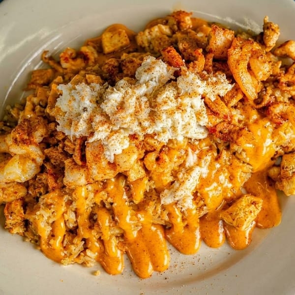 A white plate filled with rice, shrimp, chicken, orange sauce, and a dollop of white crab meat.