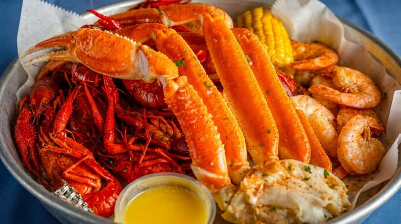 A seafood boil with crab legs, crawfish, shrimp, corn, and butter sauce in a metal bowl.
