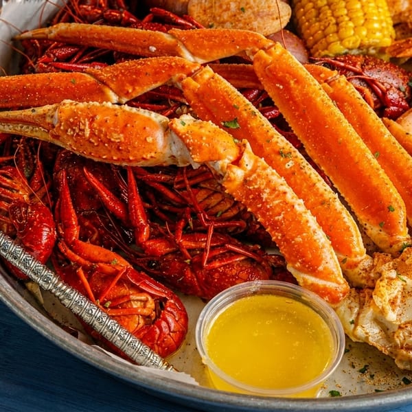 A seafood boil with crab legs, crawfish, shrimp, corn, and melted butter in a metal tray.
