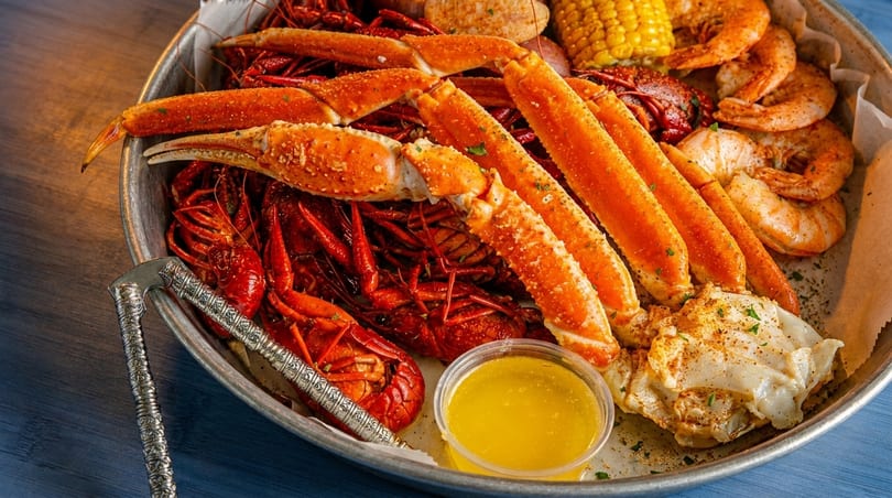 A seafood boil with crab legs, crawfish, shrimp, corn, and melted butter in a metal tray.
